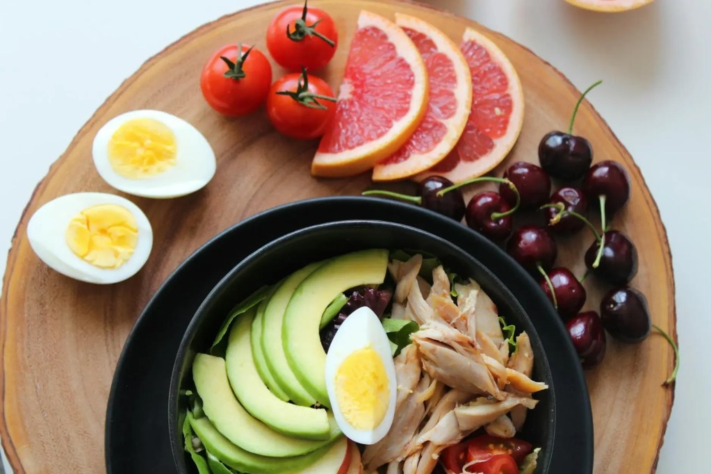 High-protein balanced mealâ€”avocado, hard-boiled eggs, shredded chicken, grapefruit slices, cherriesâ€”for sustainable nutrition